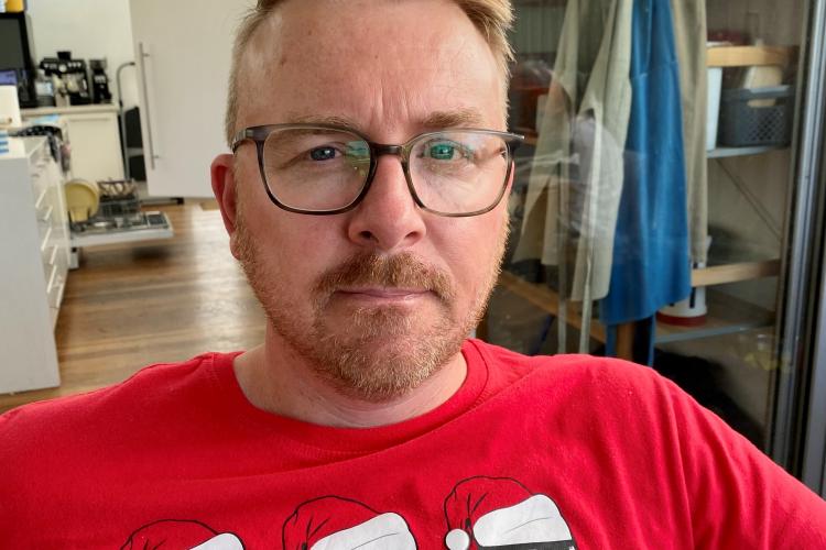 Richard - image of a white man, with beard, blue eyes and glasses wearing a red tshirt